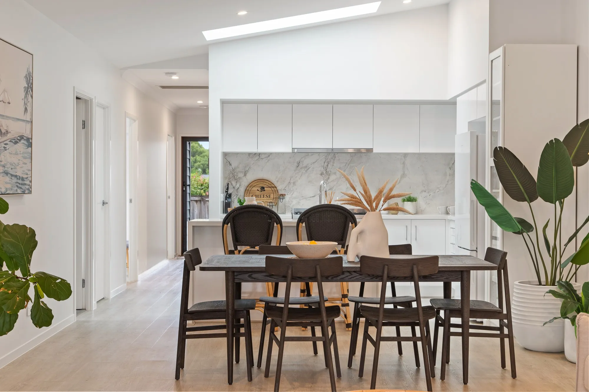 Interior of a newly built home: an open-plan kitchen and dining area with white walls and ceiling, a marble splashback, timber floors and natural light from a skylight.